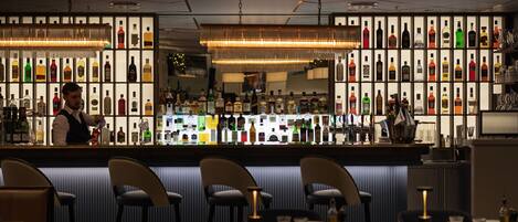 A bar area with a bartender, shelves of liquor bottles, and bar stools.