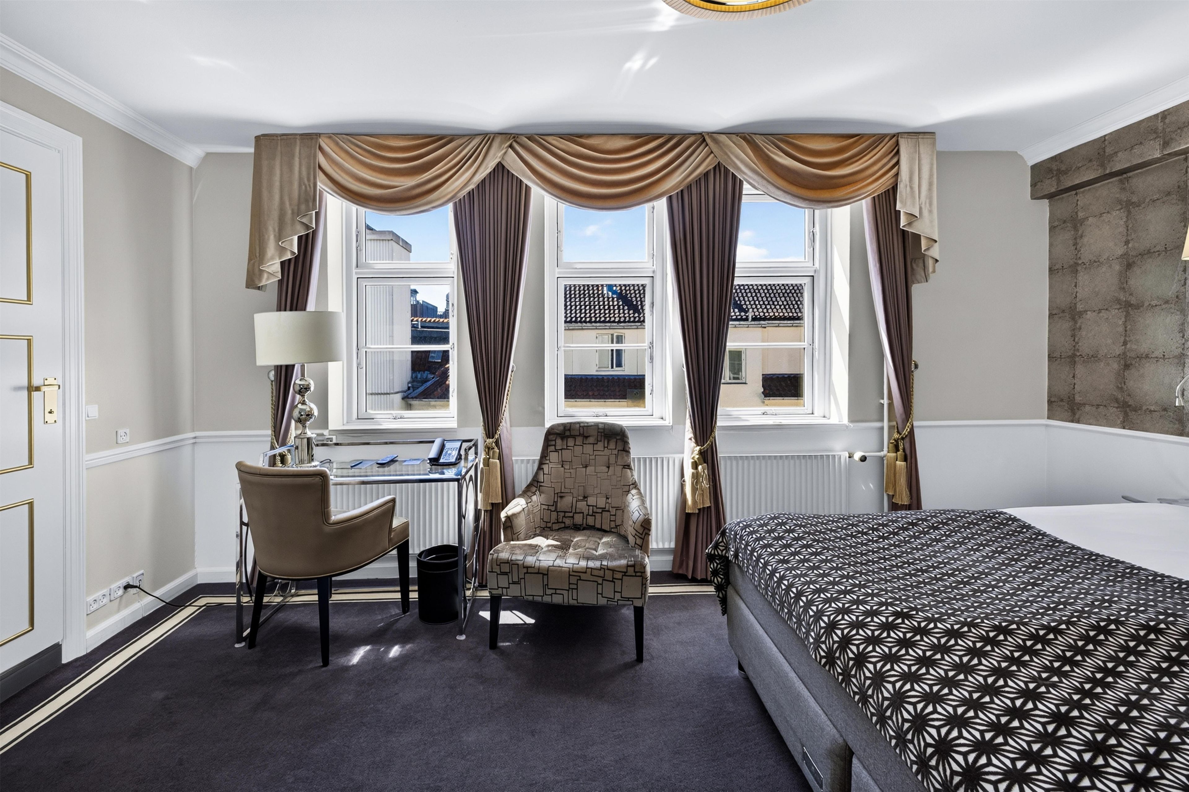 A hotel room with a bed, a desk, a chair, and a view of the outside.