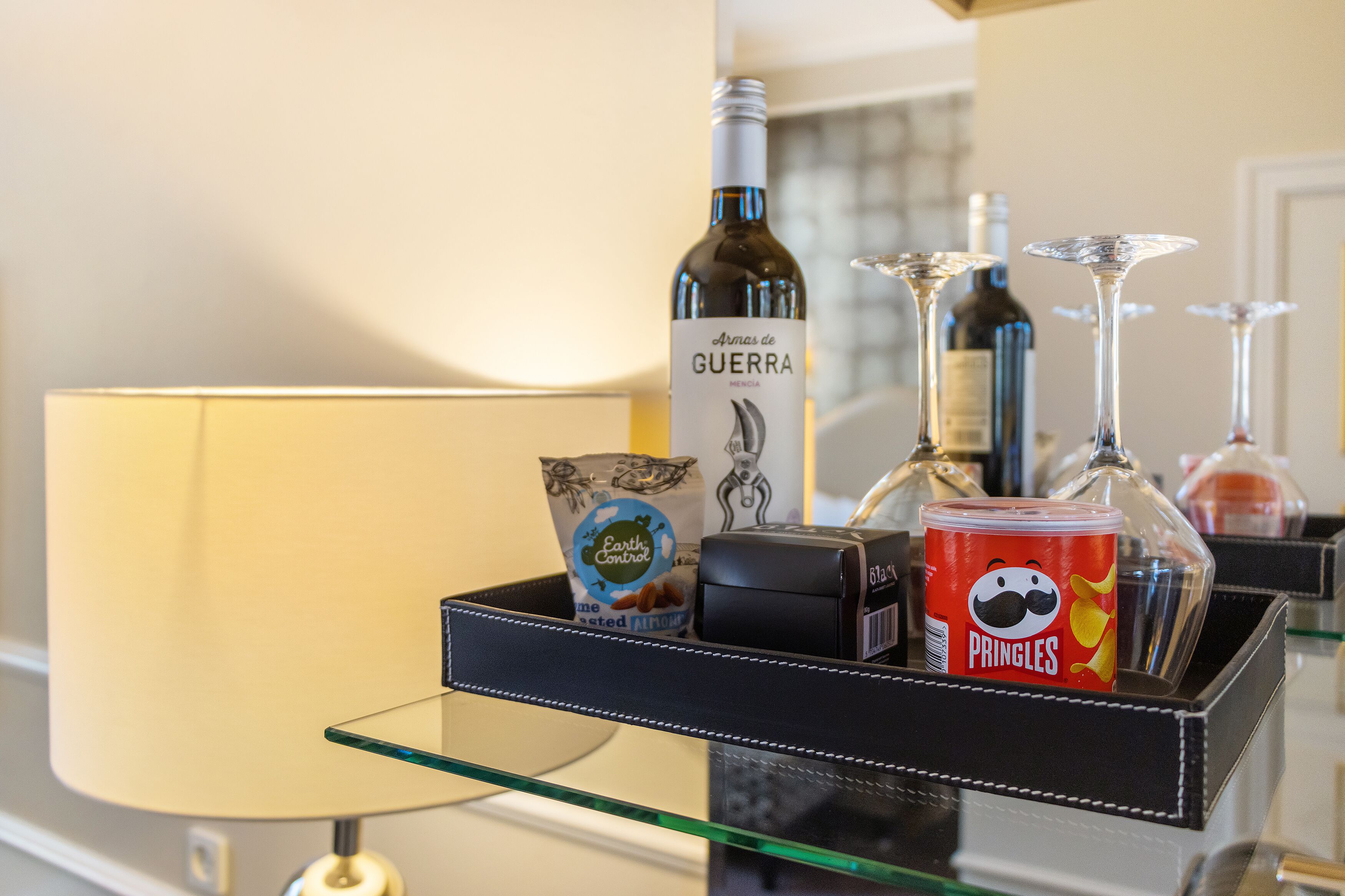 Un minibar con una botella de vino, una lata de Pringles, una bolsa de almendras y una botella de agua.