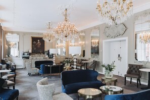 A luxurious hotel lobby with ornate chandeliers, elegant furniture, and a large mirror reflecting the room.