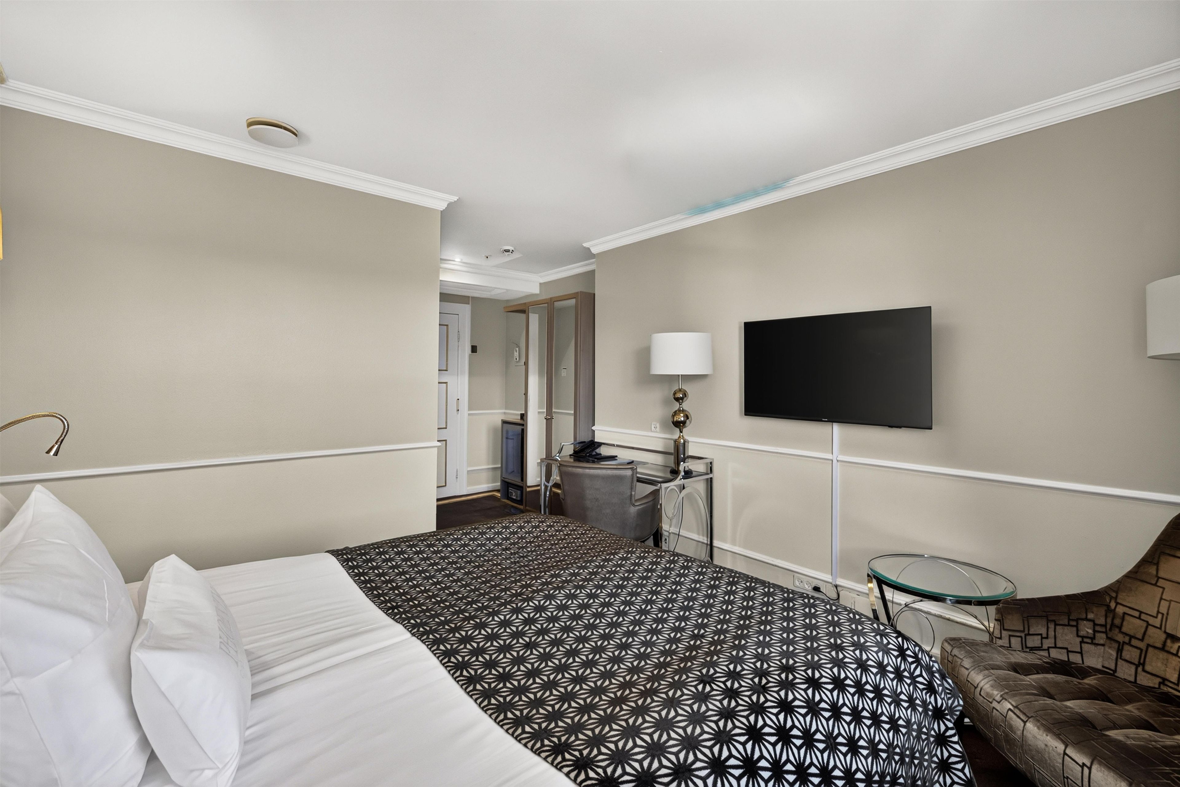 A hotel room with a bed, a TV mounted on the wall, a small table, and a chair.