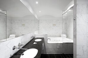 A modern bathroom with a large mirror, two sinks, a bathtub, and marble walls. - Phoenix Copenhagen (Copenhagen)