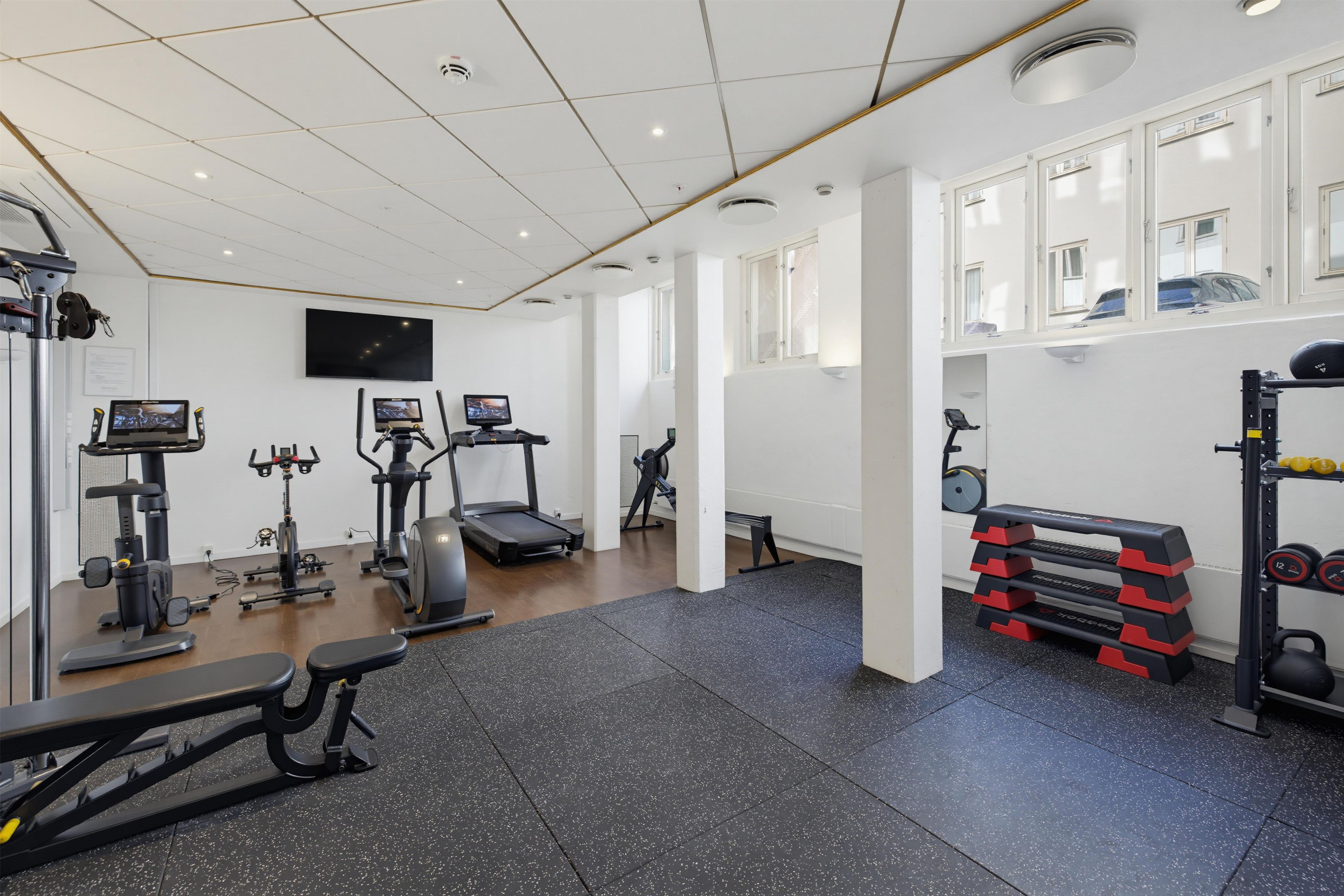 Een sportschool met diverse trainingsapparaten, een televisie en een raam met uitzicht op het exterieur.