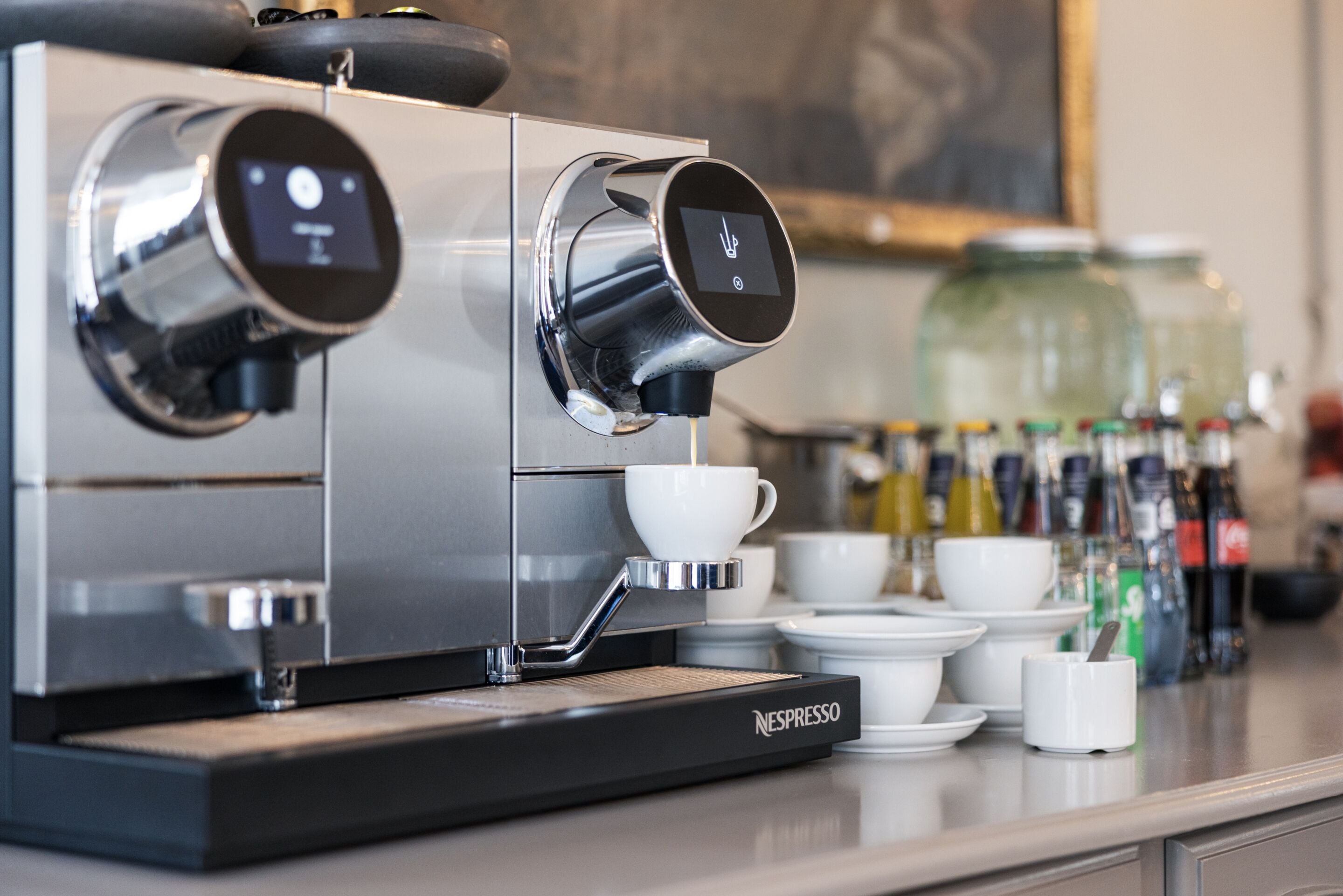 Una máquina de café espresso comercial con pantalla digital, varias tazas de café y una variedad de ingredientes en una encimera.