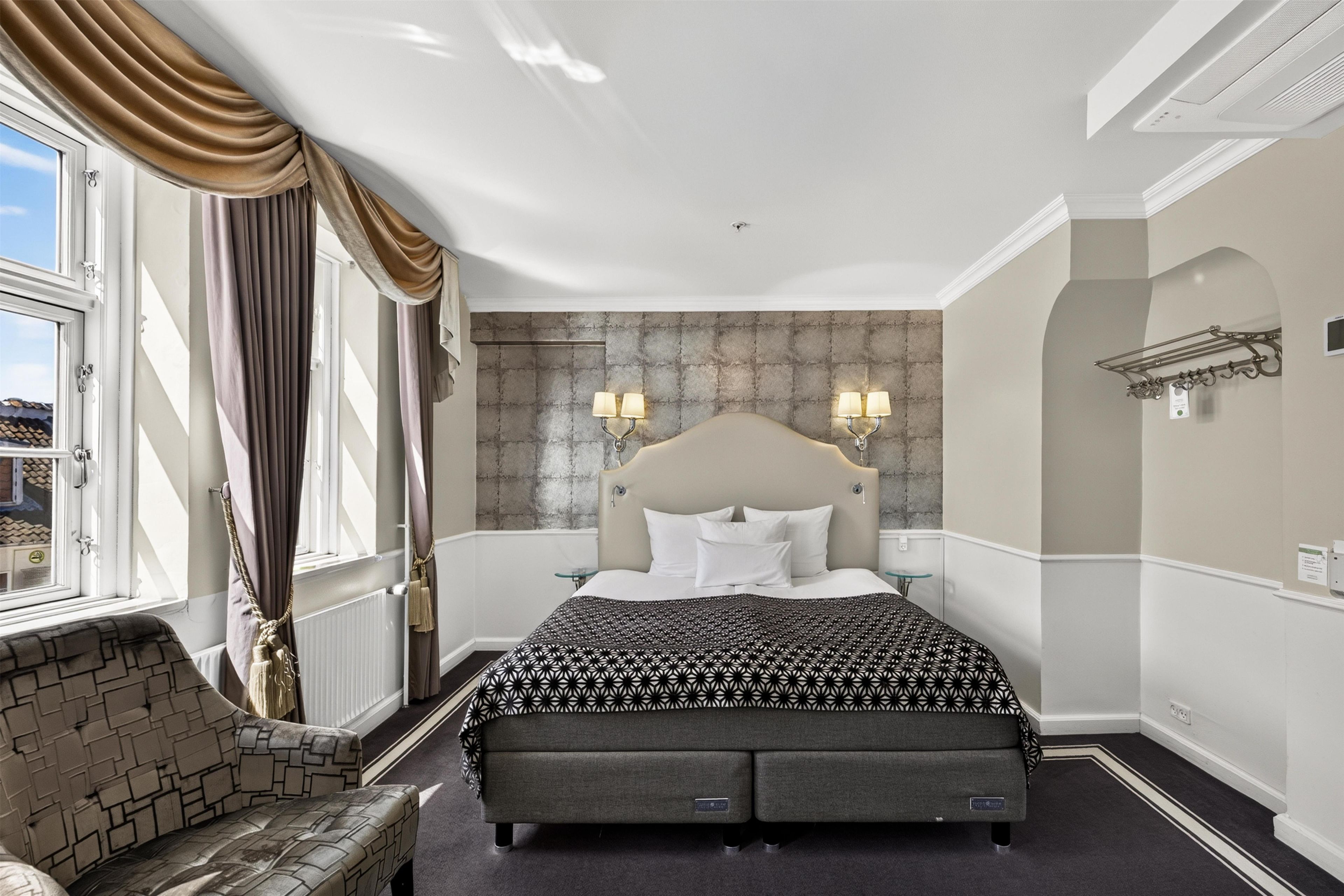 Een hotelkamer met een groot bed, een hoofdeinde, een nachtkastje, een raam met gordijnen en uitzicht op het omliggende landschap.