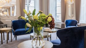 A room with a round table, a vase with flowers, and blue upholstered chairs. - Phoenix Copenhagen (Copenhagen)