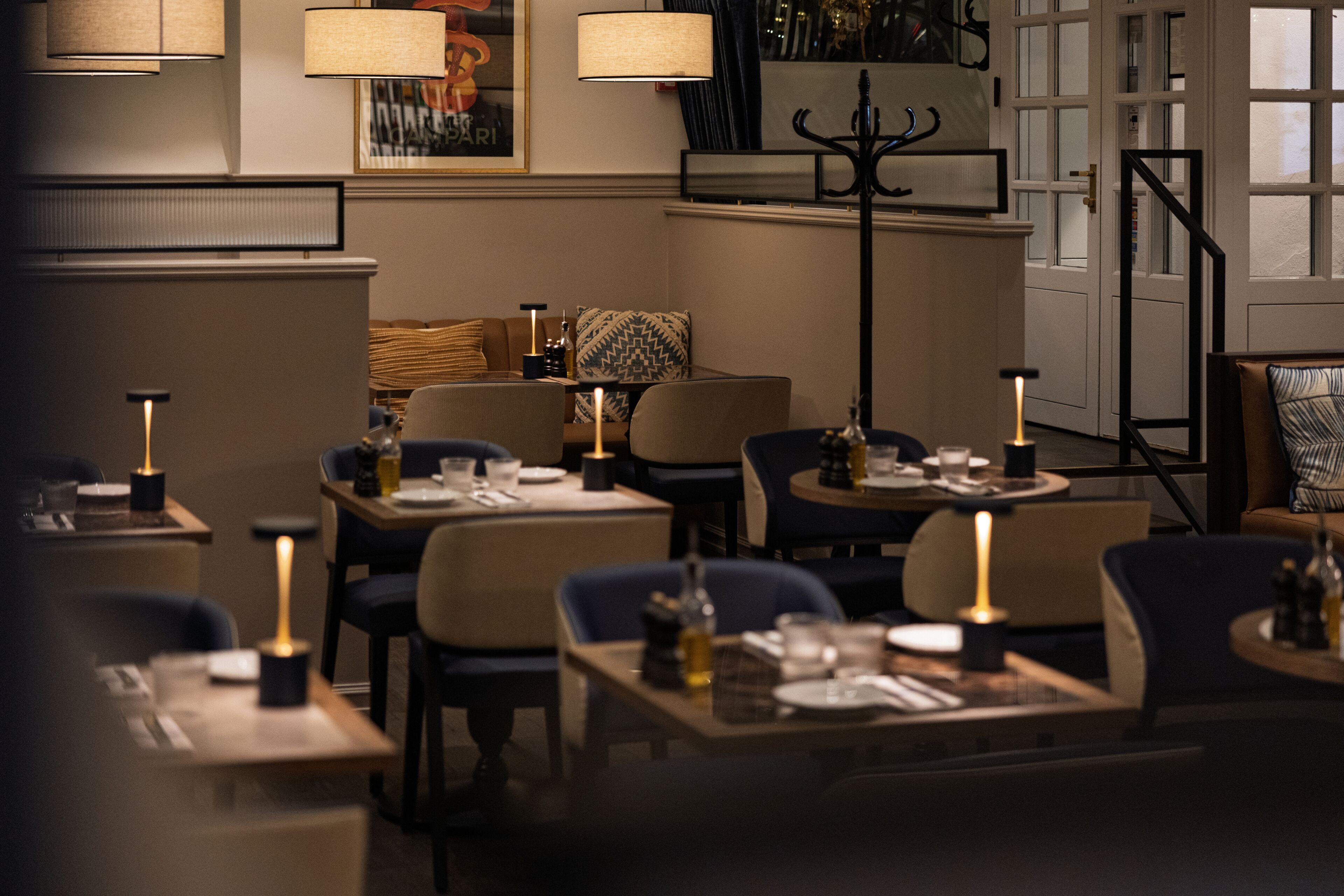 En restaurang med dämpad belysning, där borden är dukade för middag, med ljus på varje bord och en ombonad atmosfär.