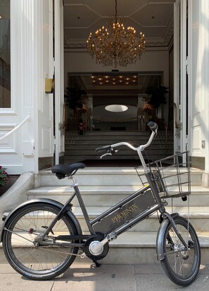A bicycle parked outside a building with a grand entrance, a chandelier, and a staircase leading to an upper level. - Phoenix Copenhagen (Copenhagen)