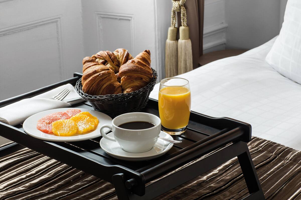 A breakfast tray with croissants, orange slices, coffee, and orange juice on a bed.