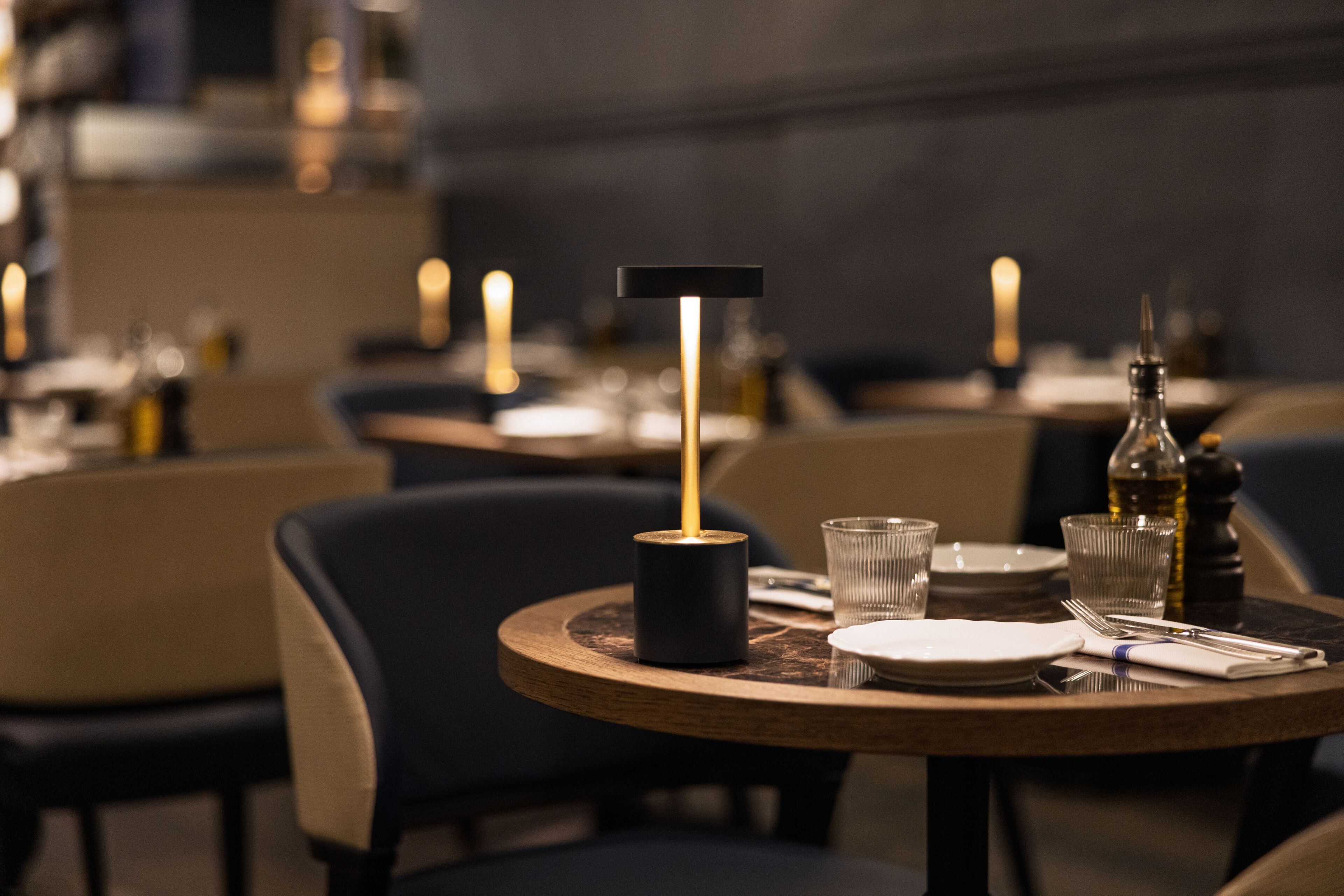 A restaurant setting with round tables, chairs, candles, and tableware.