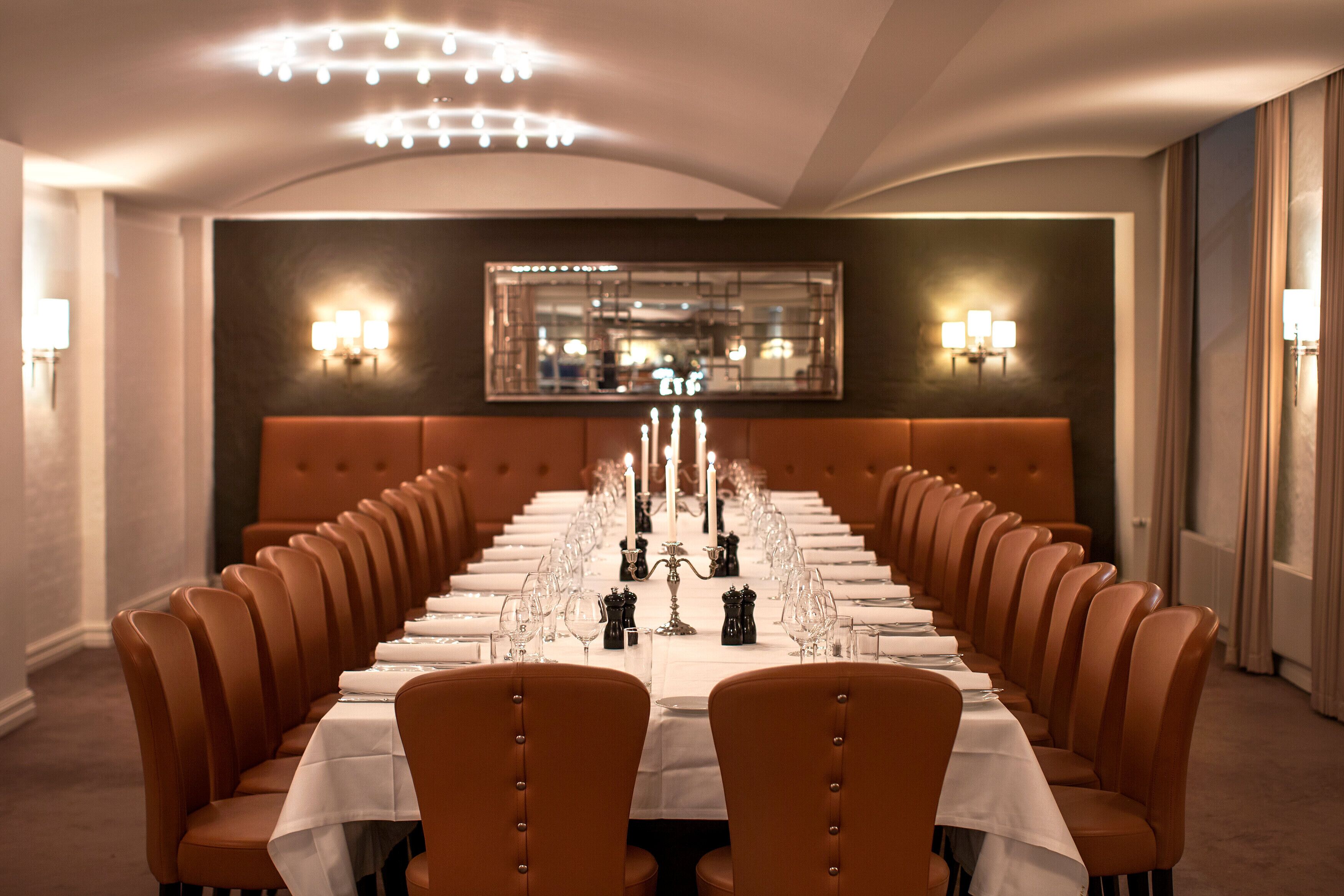 A long dining table with multiple chairs, candles, and a mirror on the wall.