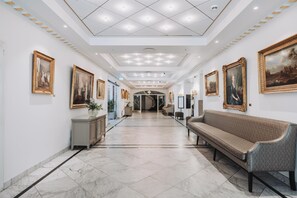 A hallway with marble flooring, a bench, and framed artwork on the walls.