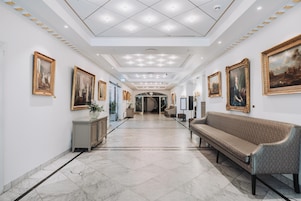 A hallway with marble flooring, a bench, and framed artwork on the walls.