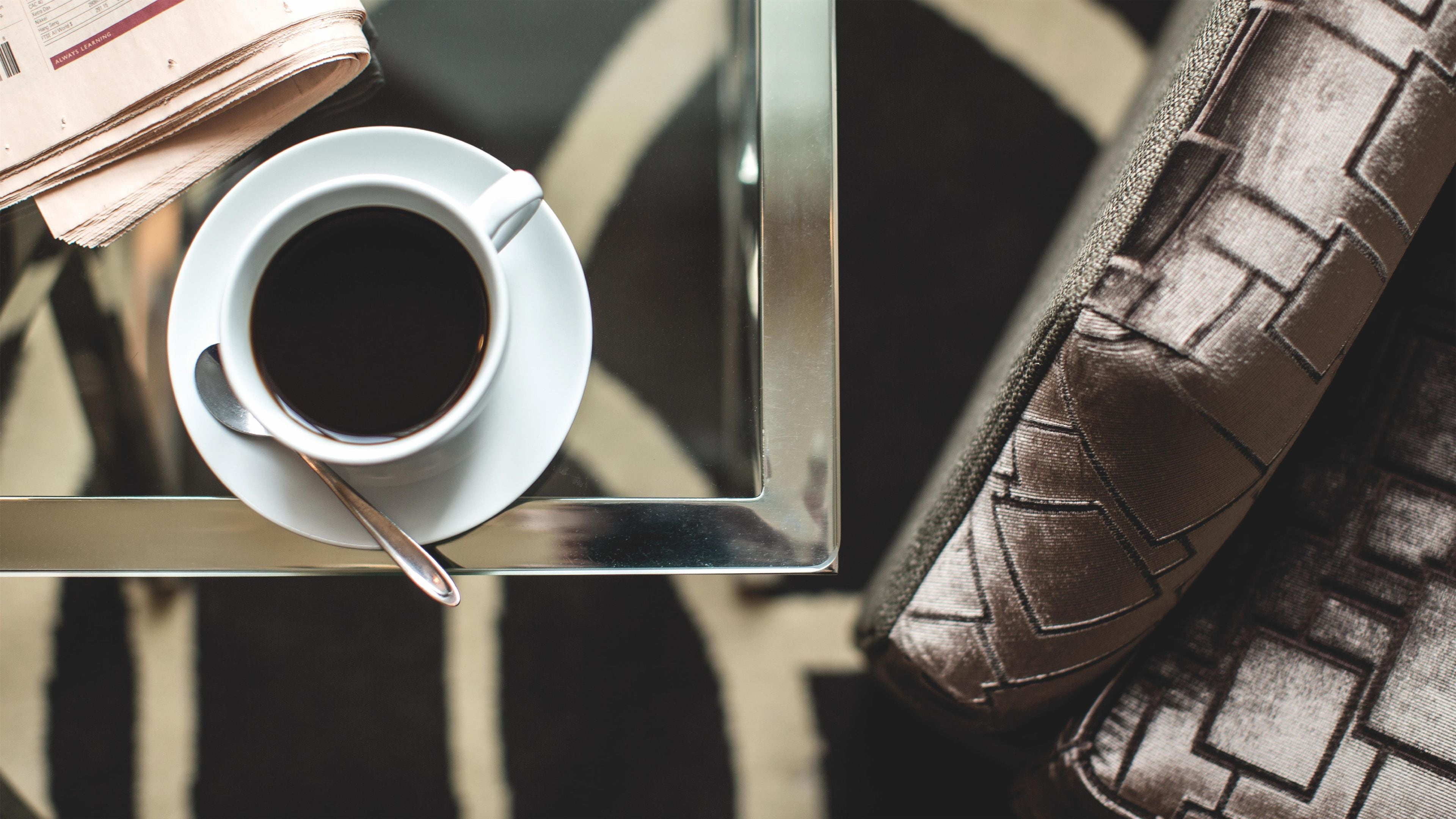 A cup of coffee on a tray with a spoon, a book, and a patterned cushion.