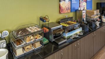 Un banco buffet con diversi cibi, tra cui pasticceria, panini e opzioni per la colazione.