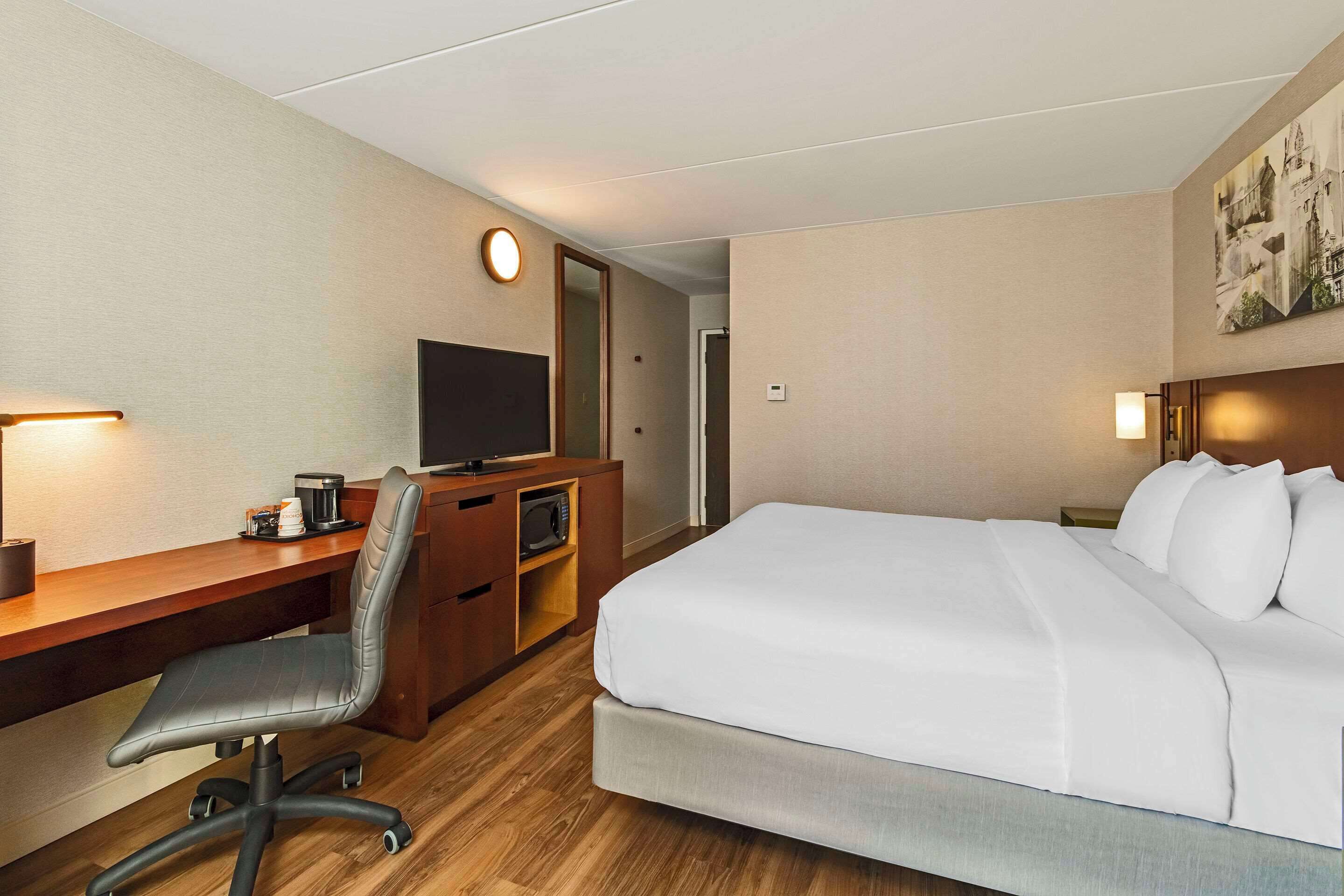 Una camera d'albergo con un letto, una scrivania, una sedia, una televisione e un'opera d'arte appesa al muro.