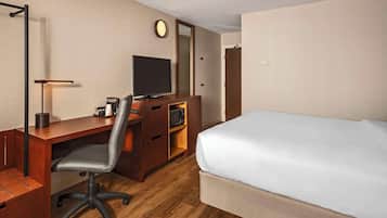 Quarto de hotel com escrivaninha de madeira, uma cadeira, cama, televisão e espelho.