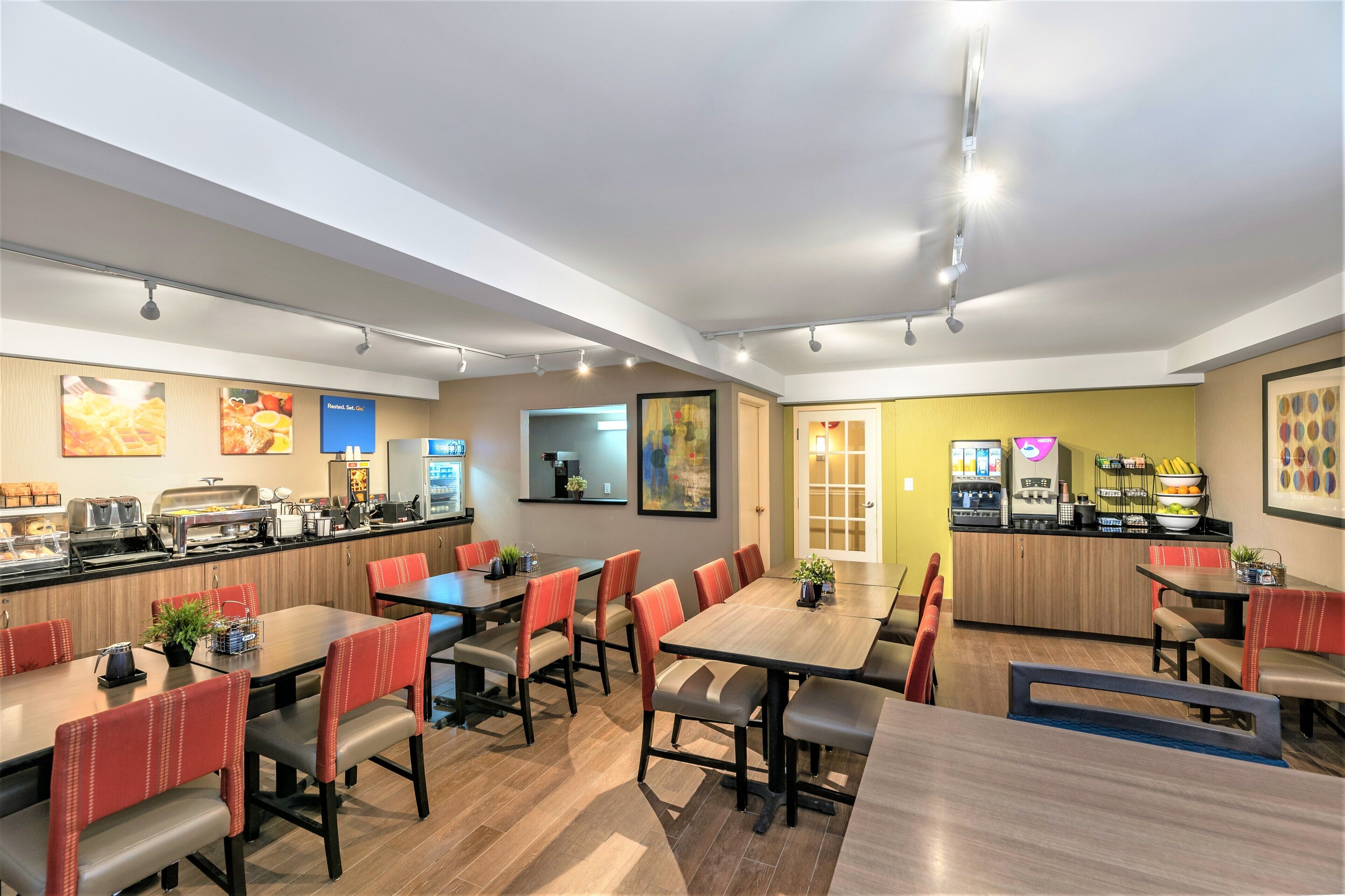 A modern restaurant with wooden tables and red chairs, a buffet area, and a bright interior.