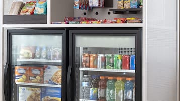 Máquina expendedora con un carrito de conveniencia encima, que contiene aperitivos y bebidas.