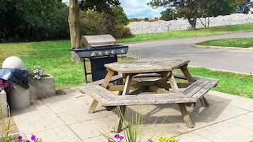 Una mesa de picnic con parrilla y basurero en un parque.