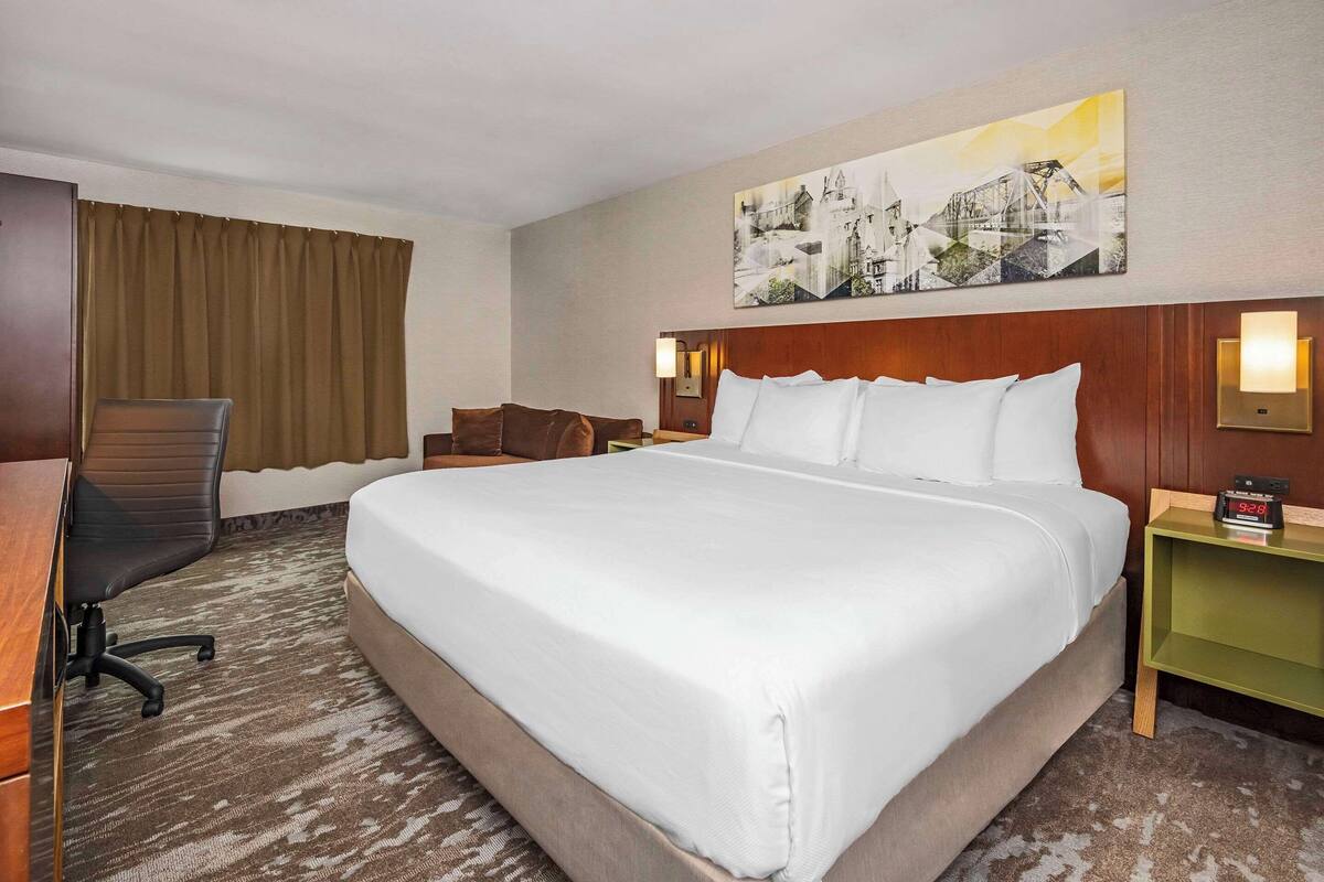 Una habitación de hotel con una cama grande, un escritorio, una silla y un cuadro en la pared.