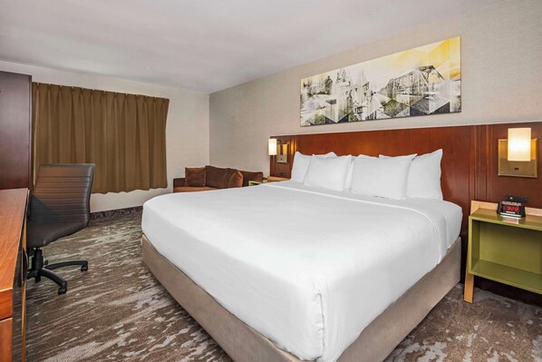 A hotel room with a large bed, a desk, a chair, and a painting on the wall.