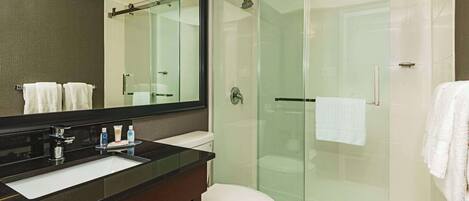 Un baño moderno con ducha envuelta en vidrio, inodoro blanco y encimera negra con lavabo.