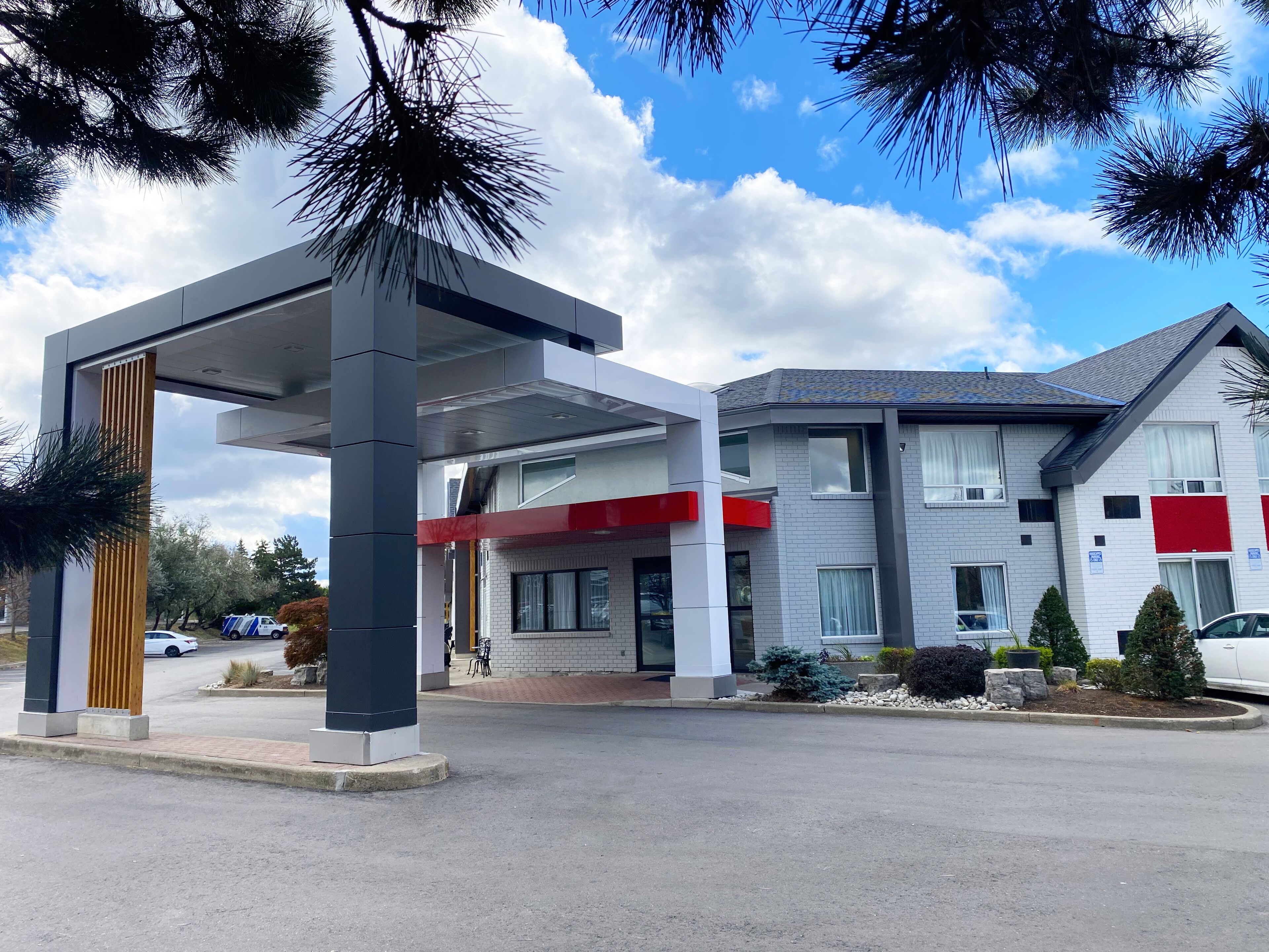 Un edificio moderno con entrada cubierta, un toldo rojo y un área de estacionamiento.
