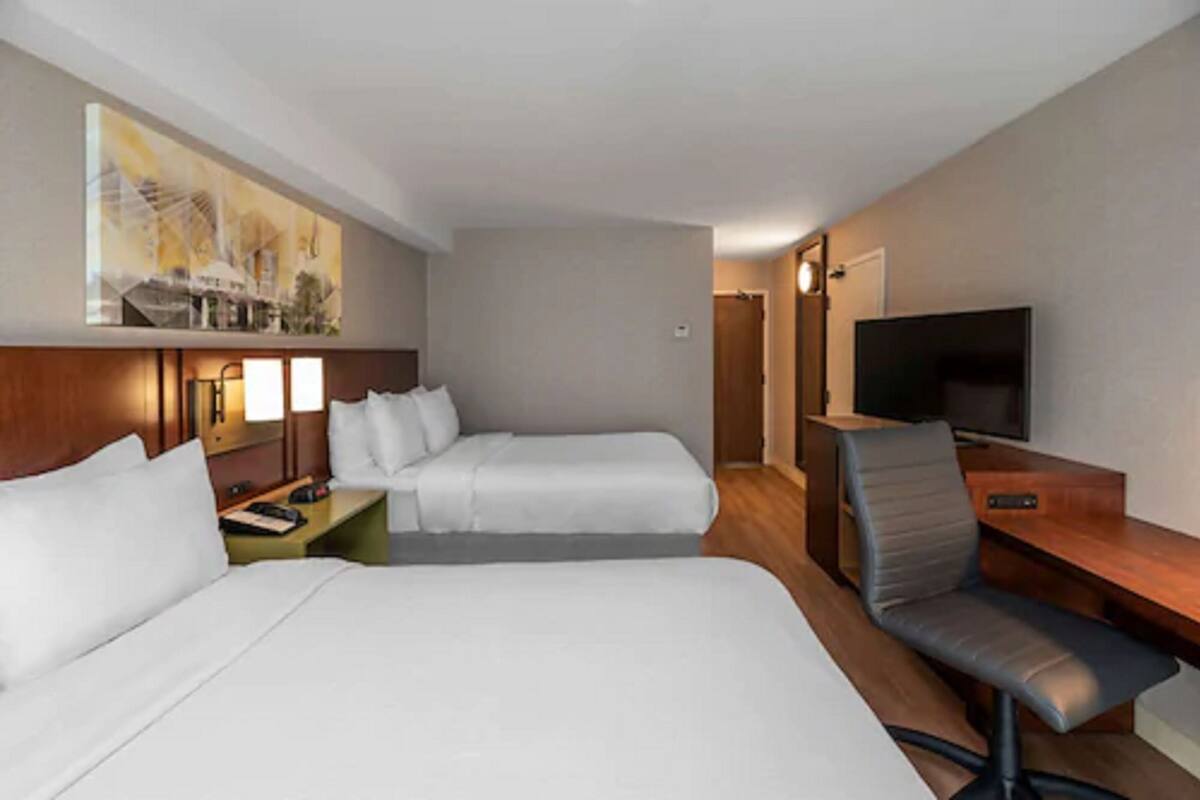 Habitación de hotel con dos camas, un escritorio con silla, televisor y un cuadro en la pared.