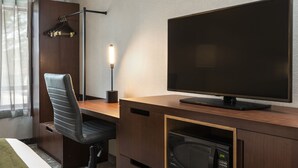 Habitación de hotel con escritorio de madera, silla de oficina negra, televisor de pantalla plana, lámpara de escritorio y microondas integrado.