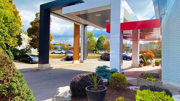 Una estación de servicio moderna con toldo cubierto, estacionamiento y áreas ajardinadas con arbustos y una planta en maceta.