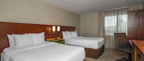 Una habitación de hotel con dos camas, un escritorio, una silla y un ventanal con cortinas.