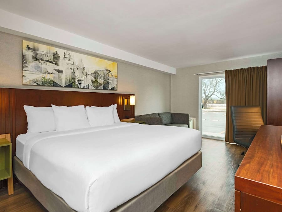 Una habitación de hotel con una cama grande, un escritorio, una silla y un cuadro en la pared.