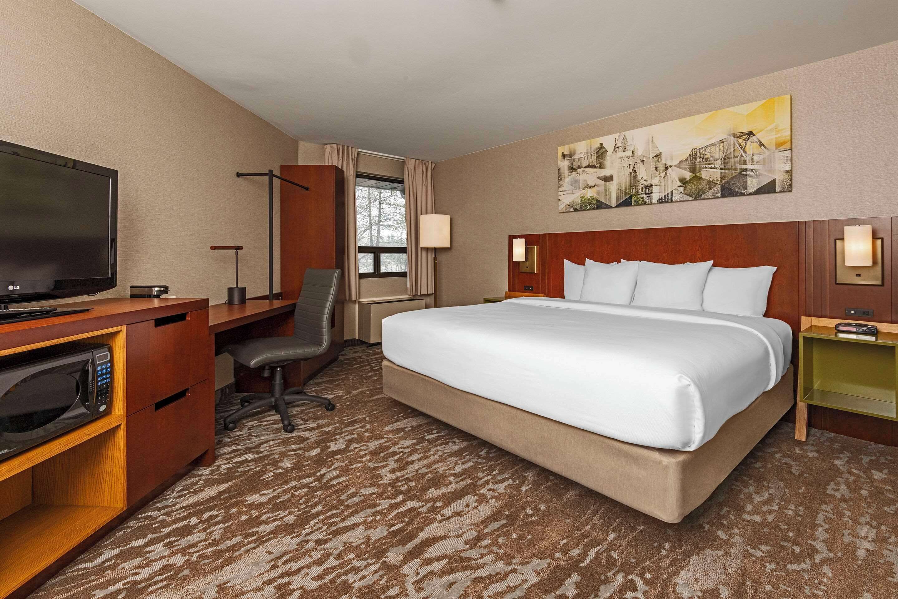 A hotel room with a large bed, a desk with a TV, a microwave, and a chair.
