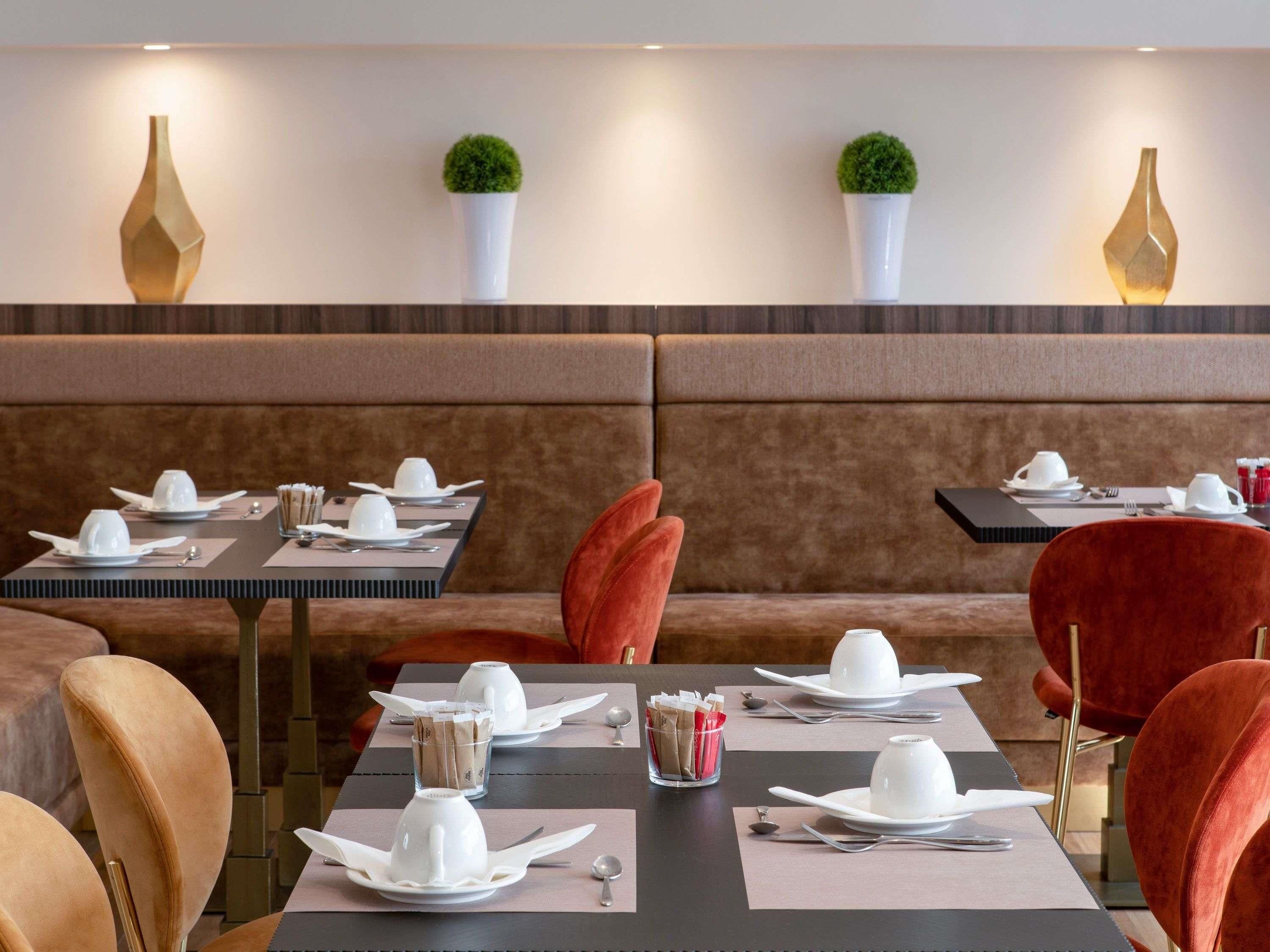 A restaurant with booths and tables, each set with white plates, cups, and cutlery.