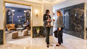 A lobby with a marble floor, a seating area with a sofa and ottoman, and a wall with a marble pattern.