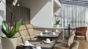 A modern dining area with tables set for service, a sofa, and a chair. - Mercure Versailles Paris Ouest (Le Chesnay-Rocquencourt)