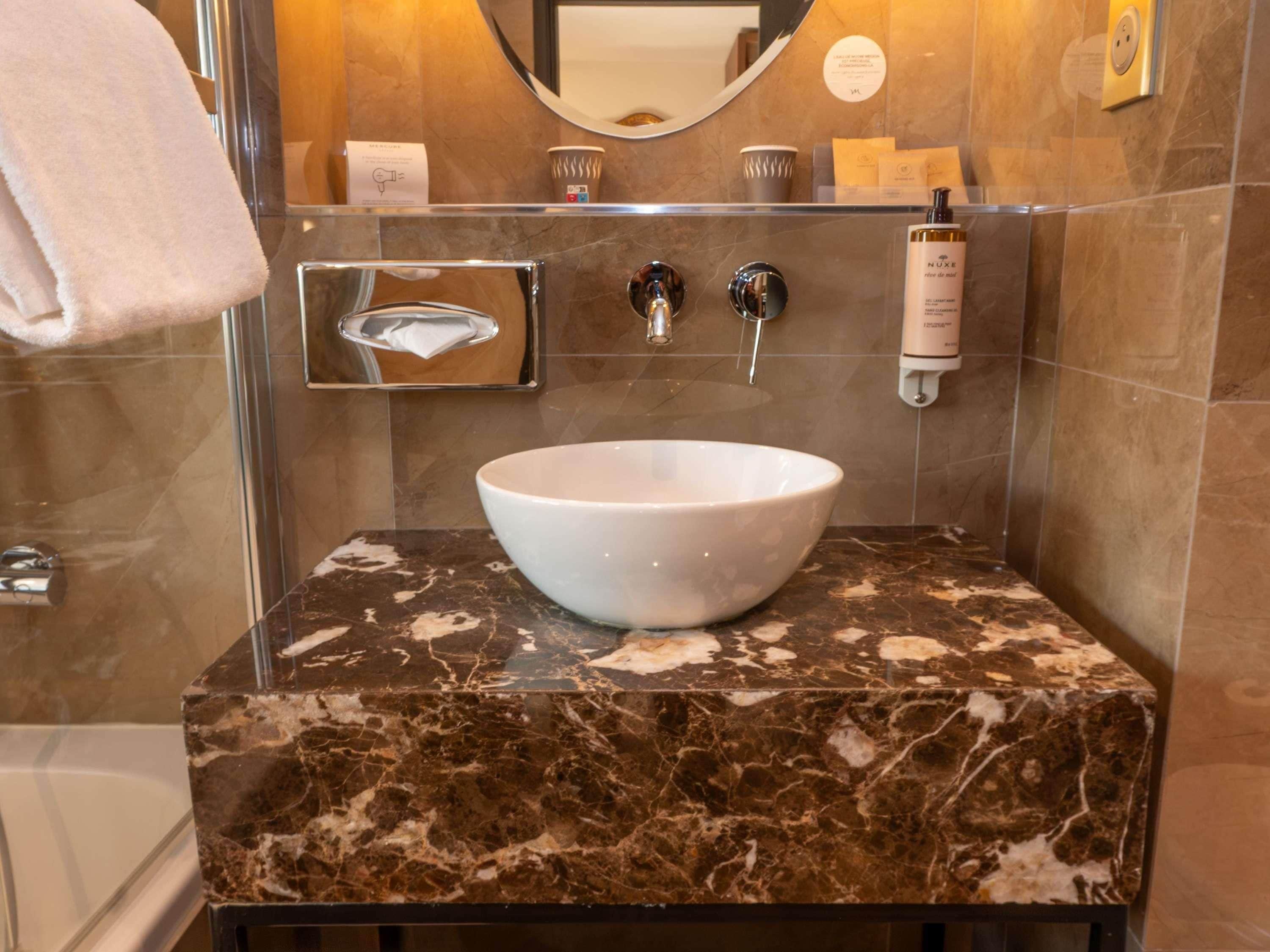 Une salle de bain avec un comptoir en marbre, un lavabo blanc, un miroir et un porte-serviettes.
