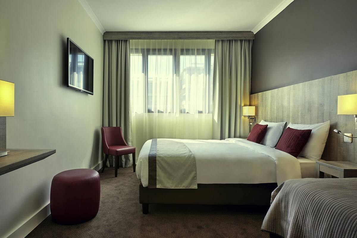 A hotel room with a bed, a chair, a desk, a lamp, and a TV.
