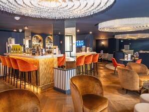 A bar area with a counter, multiple stools, and a television screen. - Mercure Versailles Paris Ouest (Le Chesnay-Rocquencourt)