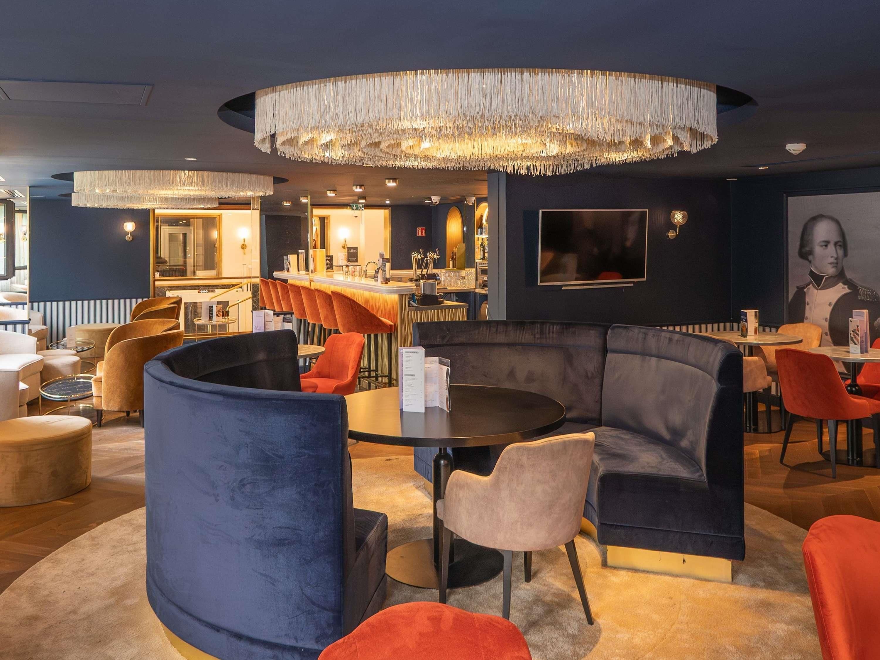 A modern lounge area with a bar, seating arrangements, and a large chandelier.