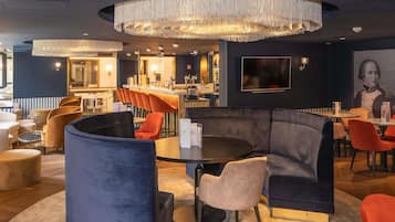 A modern lounge area with a bar, seating arrangements, and a large chandelier.