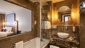 A modern bathroom with a glass-enclosed shower, a large mirror, a marble countertop, and a bathtub.