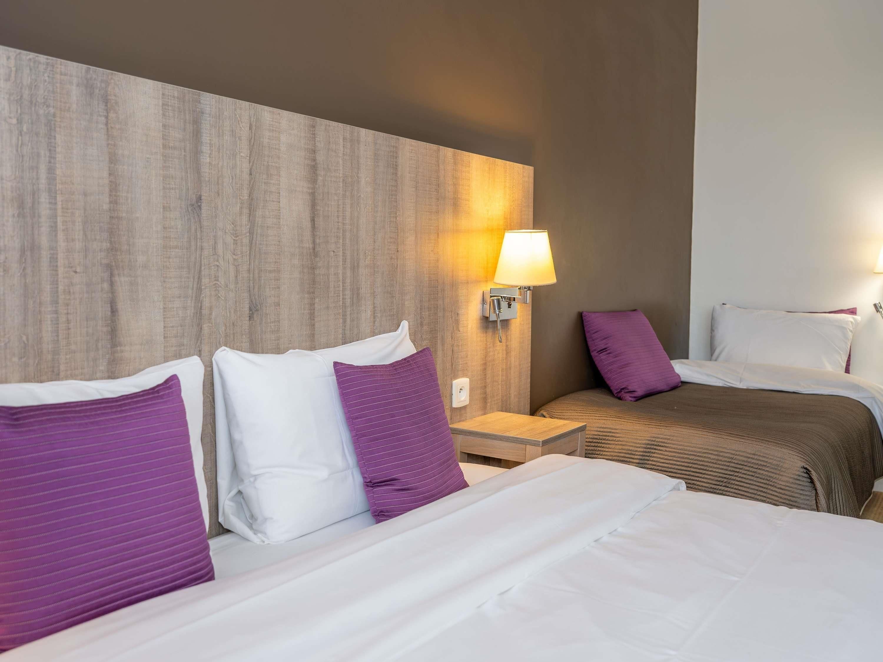 Une chambre d’hôtel avec deux lits, une table de chevet et une lampe fixée au mur.
