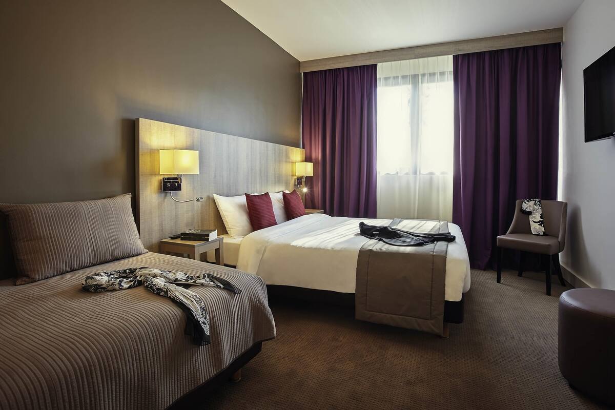 Quarto de hotel com duas camas, televisão de tela plana, escrivaninha e uma cadeira.