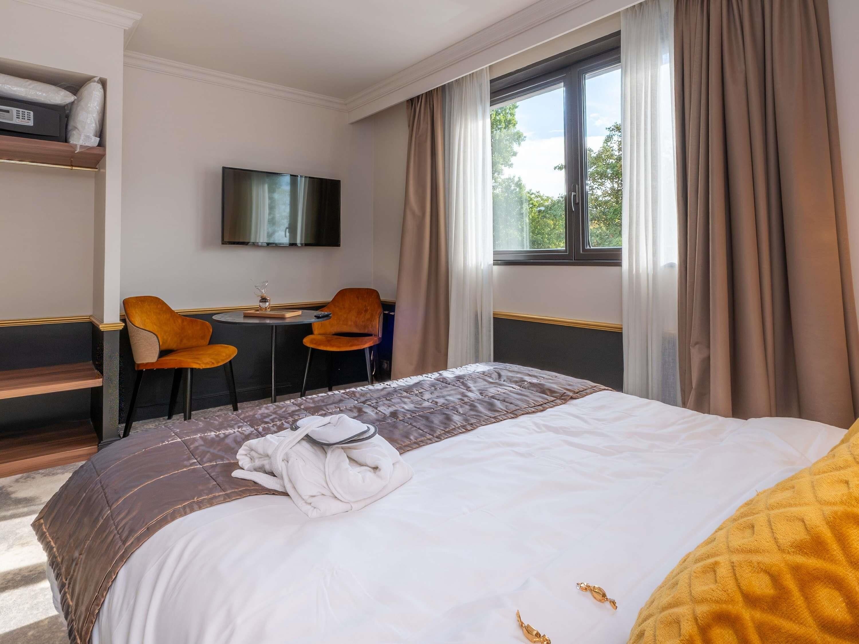 Ein Hotelzimmer mit einem Bett, einem Schreibtisch mit zwei Stühlen, einem Fernseher und einem Fenster mit Vorhängen.