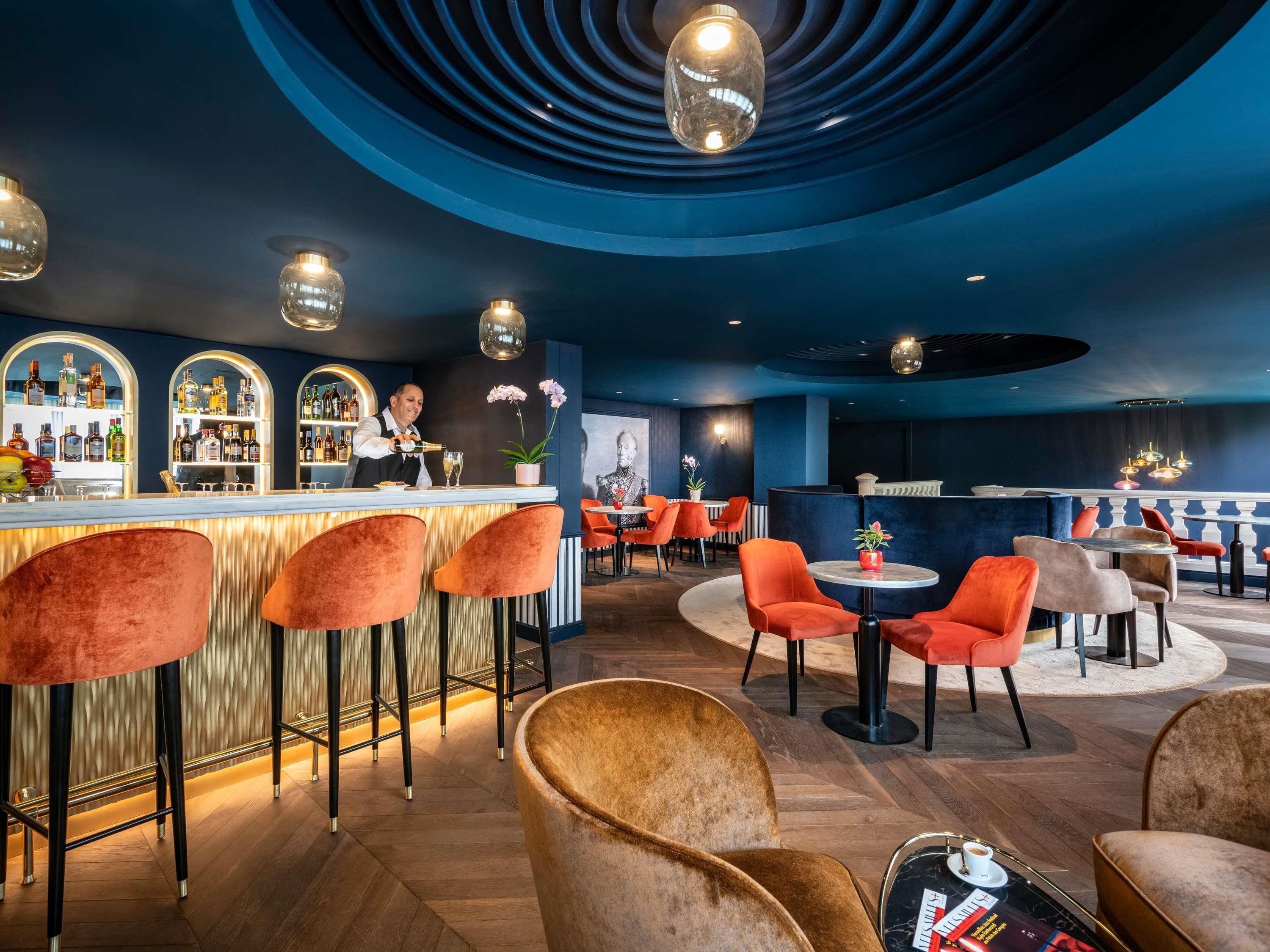 Uma área de bar com bartender, banquetas e uma variedade de garrafas.
