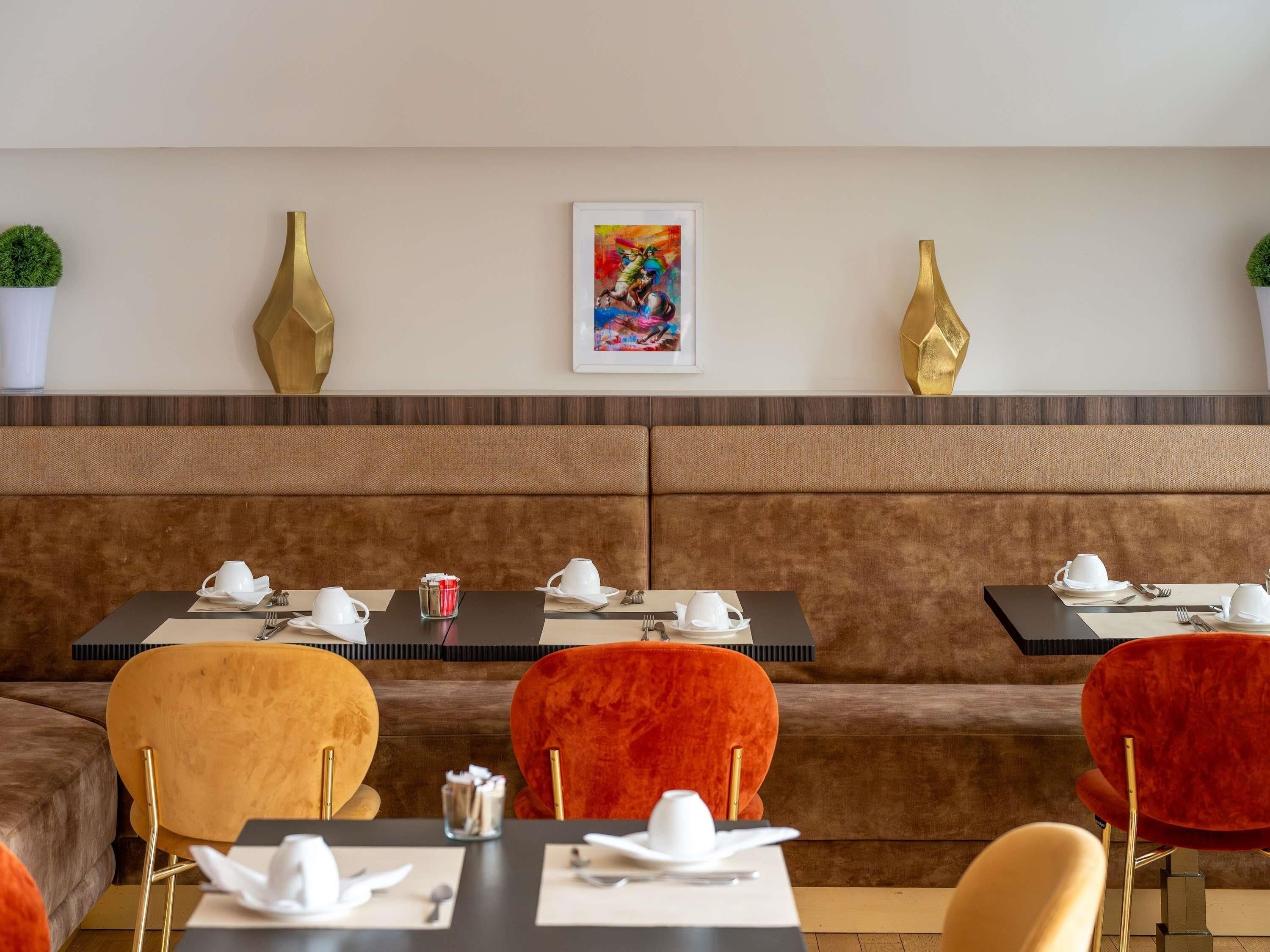 Un restaurante con una zona de asientos en banco acolchado marrón, mesas con vajilla blanca y jarrones dorados decorativos en la pared.