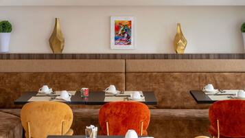 Un restaurante con una zona de asientos en banco acolchado marrón, mesas con vajilla blanca y jarrones dorados decorativos en la pared.