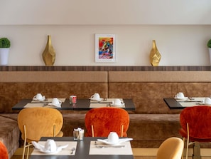 Un ristorante con un'area salotto con panche imbottite marroni, tavoli con stoviglie bianche e vasi dorati decorativi appesi al muro.